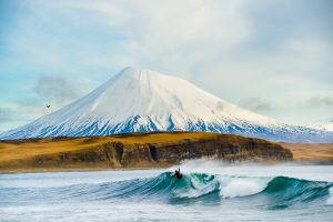 Surfer in the Aleutian Islands with Mount Vsevidof in the distant - Chris Burkard Photography