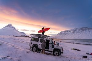 Surfer stands on vehicle unloading his surfboard in Iceland - Chris Burkard Photography