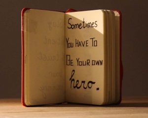 A book stands open on a desk. Hand written on the page "sometimes you have to be your own hero"